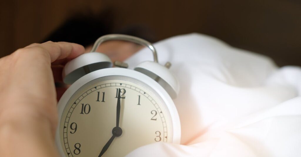 A close-up of a hand reaching for a ringing alarm clock, symbolizing waking up in the morning.